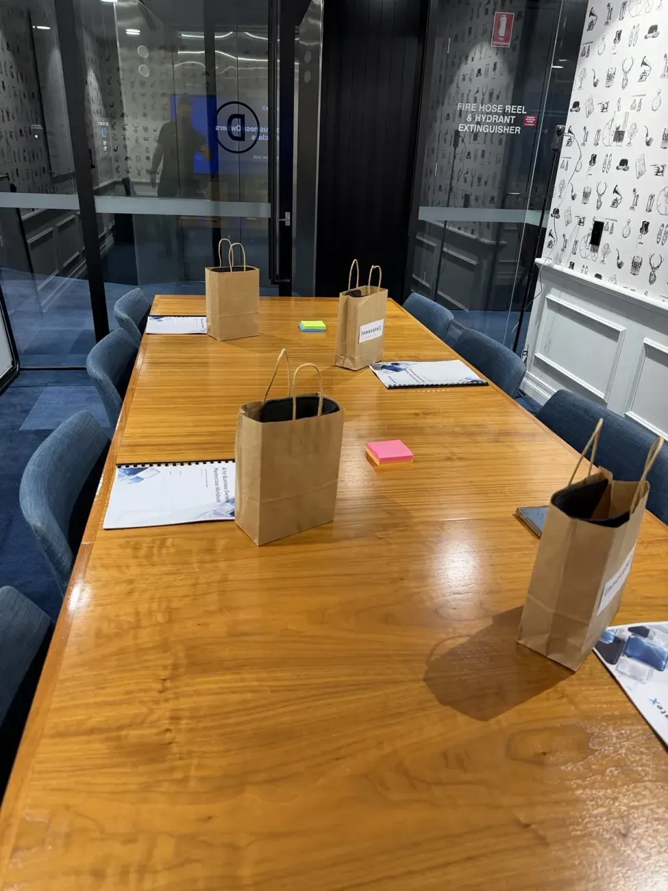 A long meeting table set with InnovateX gift bags, spiral-bound workbooks and sticky notes