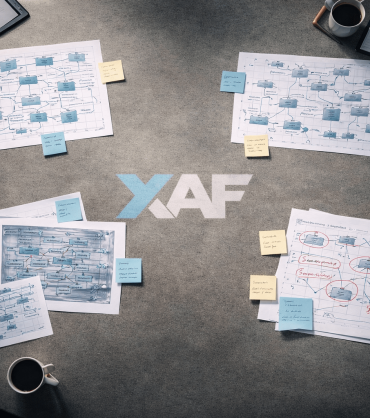 Overhead view of a workspace table covered with separate clusters of architecture diagrams, sticky notes, and whiteboard sketches with visible gaps between each domain's work.