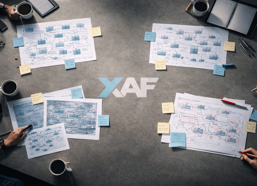 Overhead view of a workspace table covered with separate clusters of architecture diagrams, sticky notes, and whiteboard sketches with visible gaps between each domain's work.